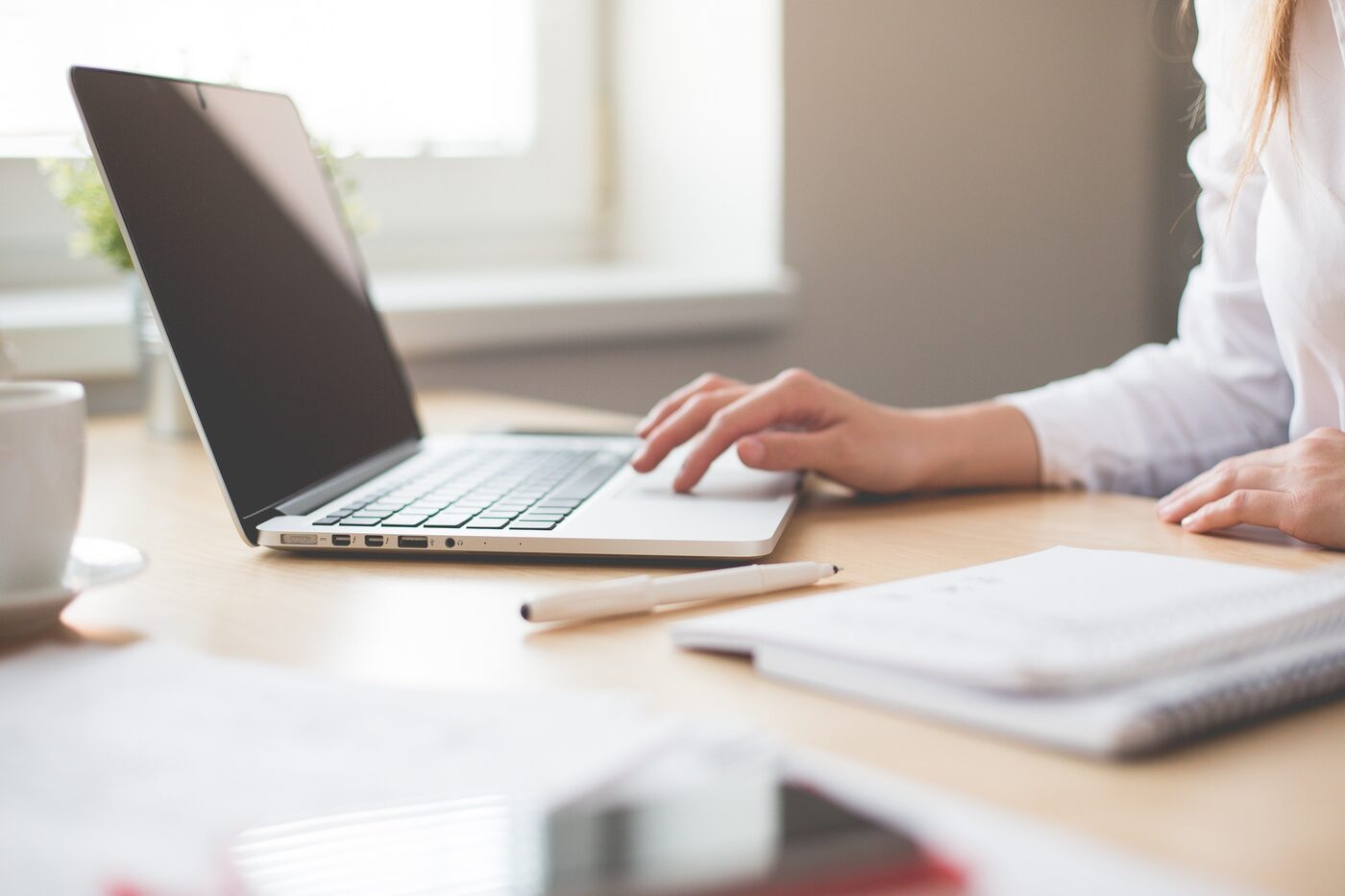 Personne travaillant sur un ordinateur portable a un bureau, avec un carnet, un stylo et une tasse de cafe